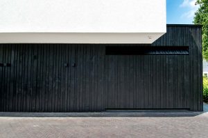 Zwarte-houten-garagedeur-verticaal-geprofileerd-in-drie-breedtes-gelijk-met-gevel-1