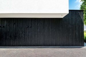 Zwarte-houten-garagedeur-verticaal-geprofileerd-in-drie-breedtes-gelijk-met-gevel